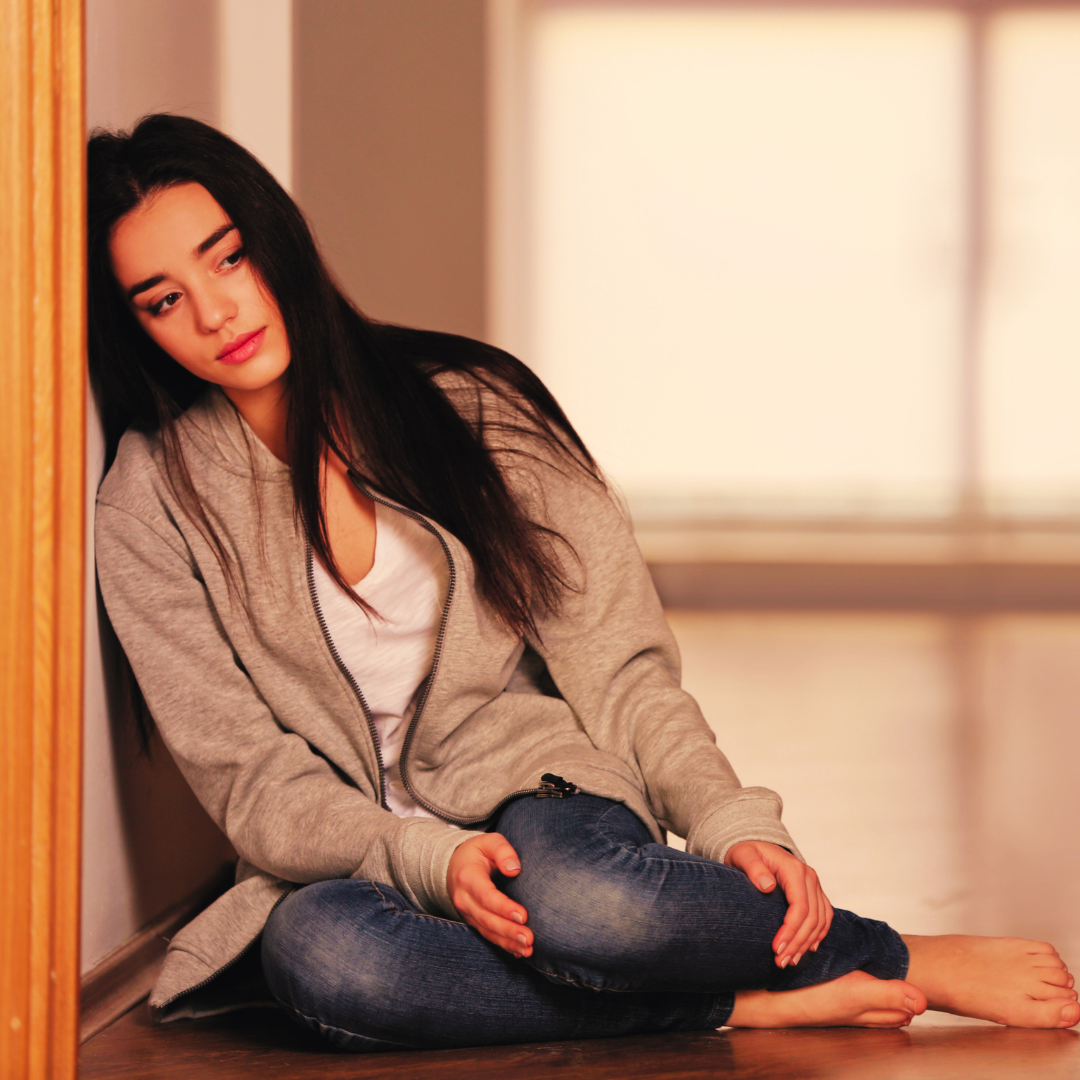 Woman sitting alone against a closed door, representing emotional withdrawal and the shutdown response in adults with early attachment wounds