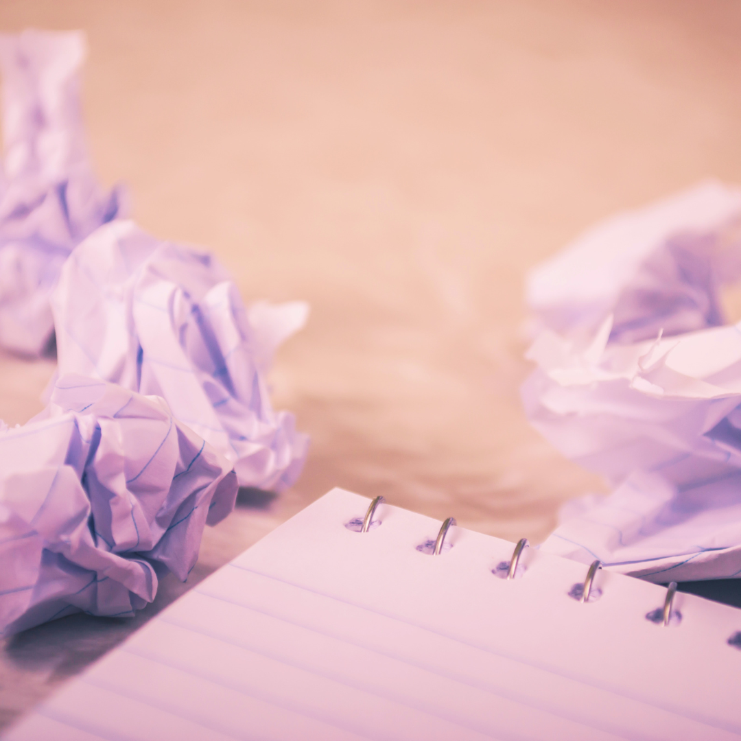 A blank piece of paper surrounded by crumpled discarded drafts, representing the exhausting cycle of perfectionism rooted in the fear of getting it wrong